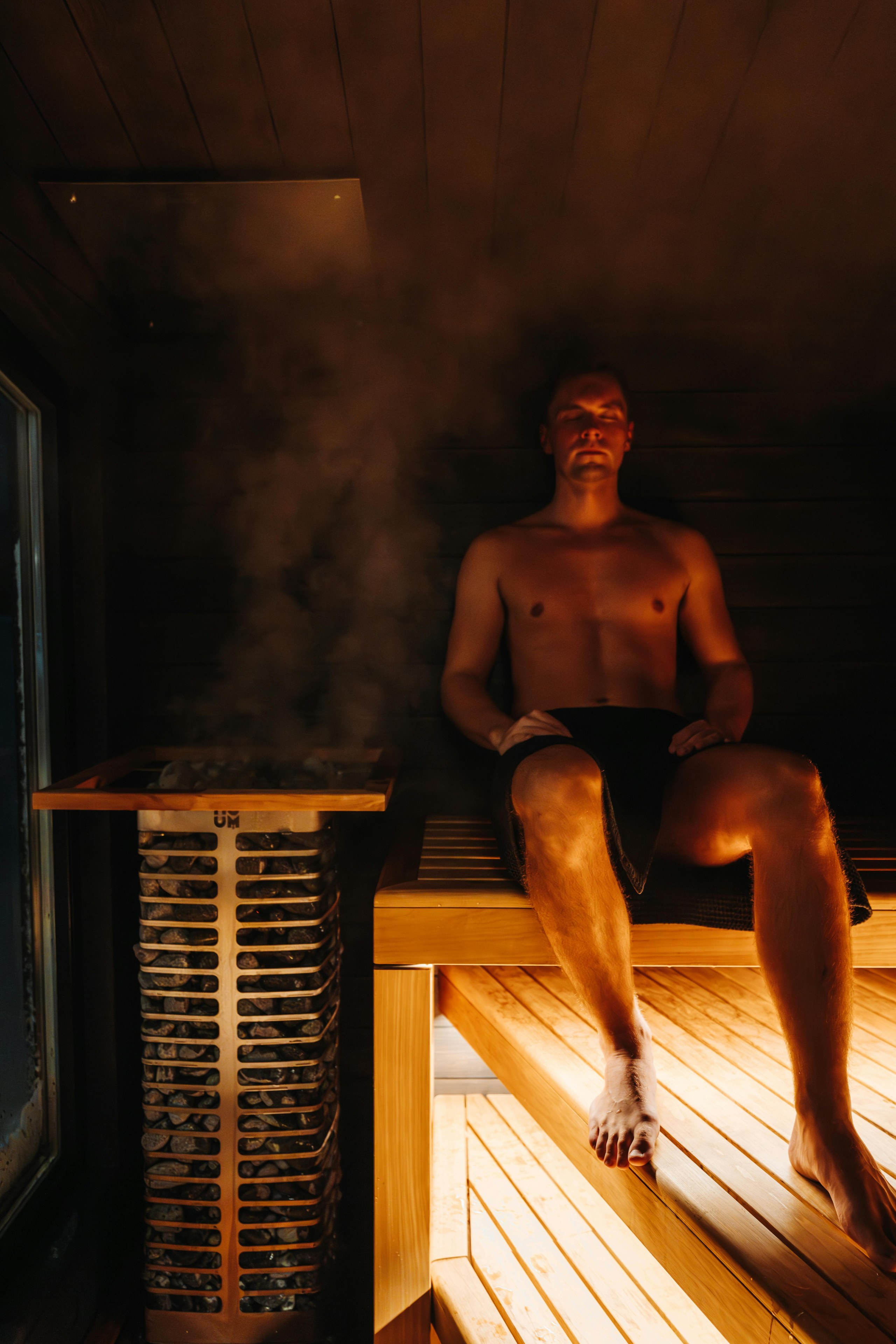 En man sitter i en bastu vid ett ångande bastuaggregat