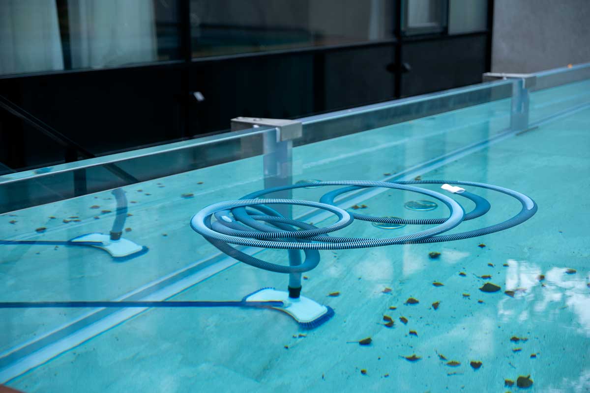 Rengöringsborste nedsänkt i utomhuspoolens vatten, för rengöring av botten och väggar, pool full av löv och andra tecken på försummelse - smuts