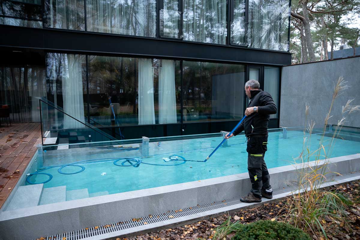 Utomhuspool med grumligt och smutsigt vatten, bruna fläckar och smuts syns på ytan, en person som står bredvid poolen