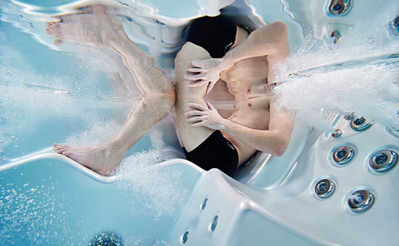 Kvinna som kopplar av i en ergonomisk solstol i en USSPA-spapool med hydromassagestrålar i drift